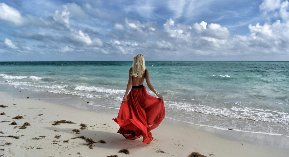 A woman in a flowing red dress enjoys a walk on a scenic Bahamas beach.